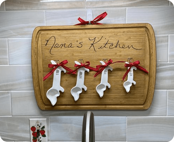 A wooden cutting board with four white spoons hanging on it.